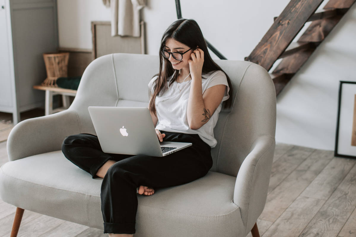 A woman sitting on a sofa using a laptop with earphones